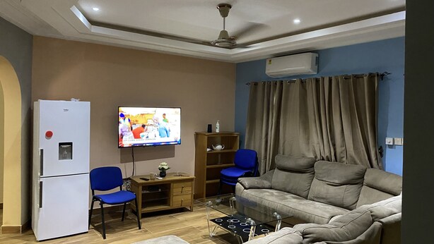 A living room with a sofa, two chairs, a TV, a refrigerator, and a wooden cabinet. - Oyibi New Furnished House - Charming 3 Bedroom (Accra)