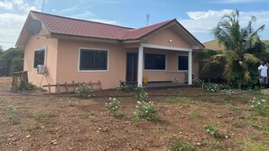 A single-story house with a red-tiled roof, large windows, and a satellite dish. - Oyibi New Furnished House - Charming 3 Bedroom (Accra)