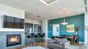 A modern living room with a fireplace, a dining area, and a kitchen in the background.