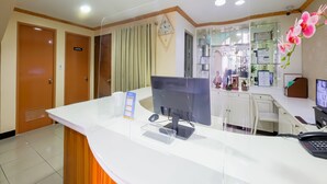 A reception area with a white counter, computer, and phone. There are two doors, one with a sign, and a window with curtains. - OYO 836 E & H Residences (Parañaque)