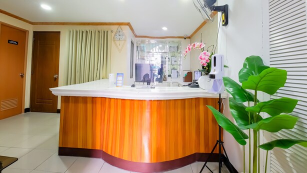 A reception area with a wooden counter, a clock, a computer, and a potted plant. - OYO 836 E & H Residences (Parañaque)