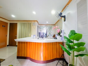 Una zona reception con un bancone in legno, un orologio, un computer e una pianta in vaso.