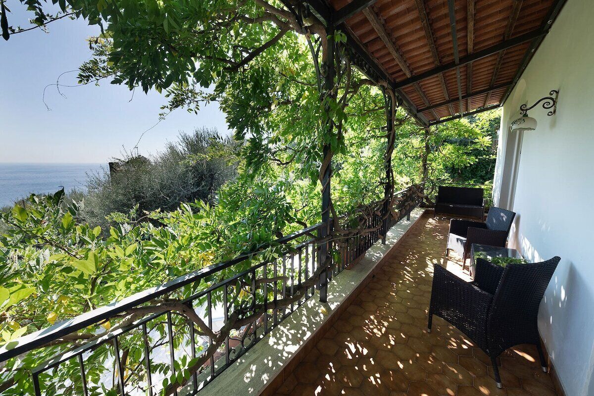A covered balcony with wicker furniture, overlooking a lush landscape and the sea.