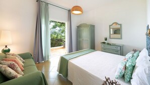 Un dormitorio con cama, un sofá verde, cómoda, lámpara y ventana con cortinas.