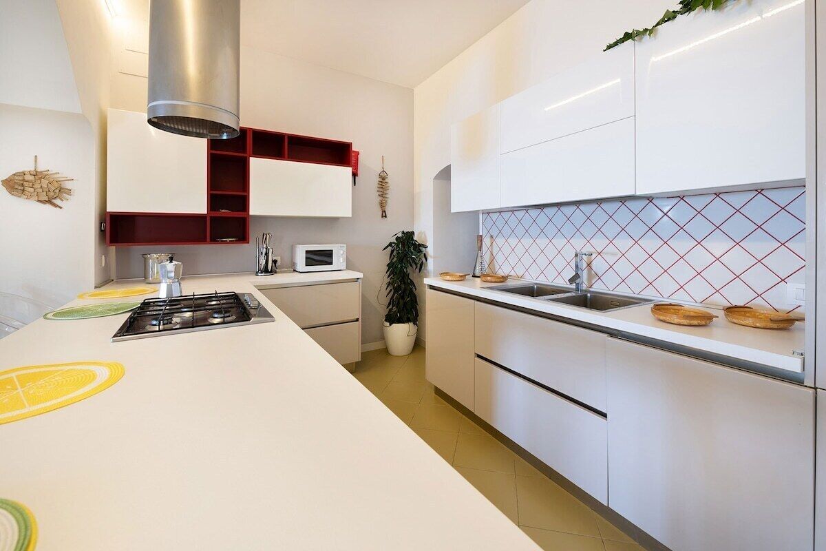 Una cocina moderna con armarios blancos, una campana extractora de acero inoxidable, un microondas y un lavamanos.