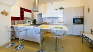 Una cocina moderna con una isla central, taburetes de bar, horno empotrado y una unidad de almacenamiento roja.
