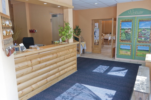 A reception area with a wooden reception desk, a potted plant, and a door with a scenic painting.