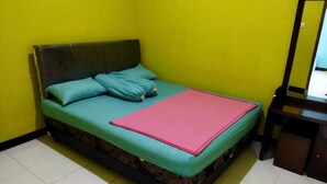 A single bed with a green mattress and teal pillows, a pink blanket, and a dark headboard in a room with yellow walls and a tiled floor.