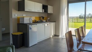A modern kitchen with white cabinets, a built-in microwave, and a coffee maker. There is a dining table with chairs and a view of a green landscape through a large window. - Le Clos de l'Archeneau - Apartment 75m2 - 6 people (Bressuire)