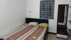 A small, single-bed room with a striped bedspread, a window with metal bars, a mirror, and a wardrobe. - wellmark resort room 1, Hall 1,  bathroom 1 (jambavanodai)
