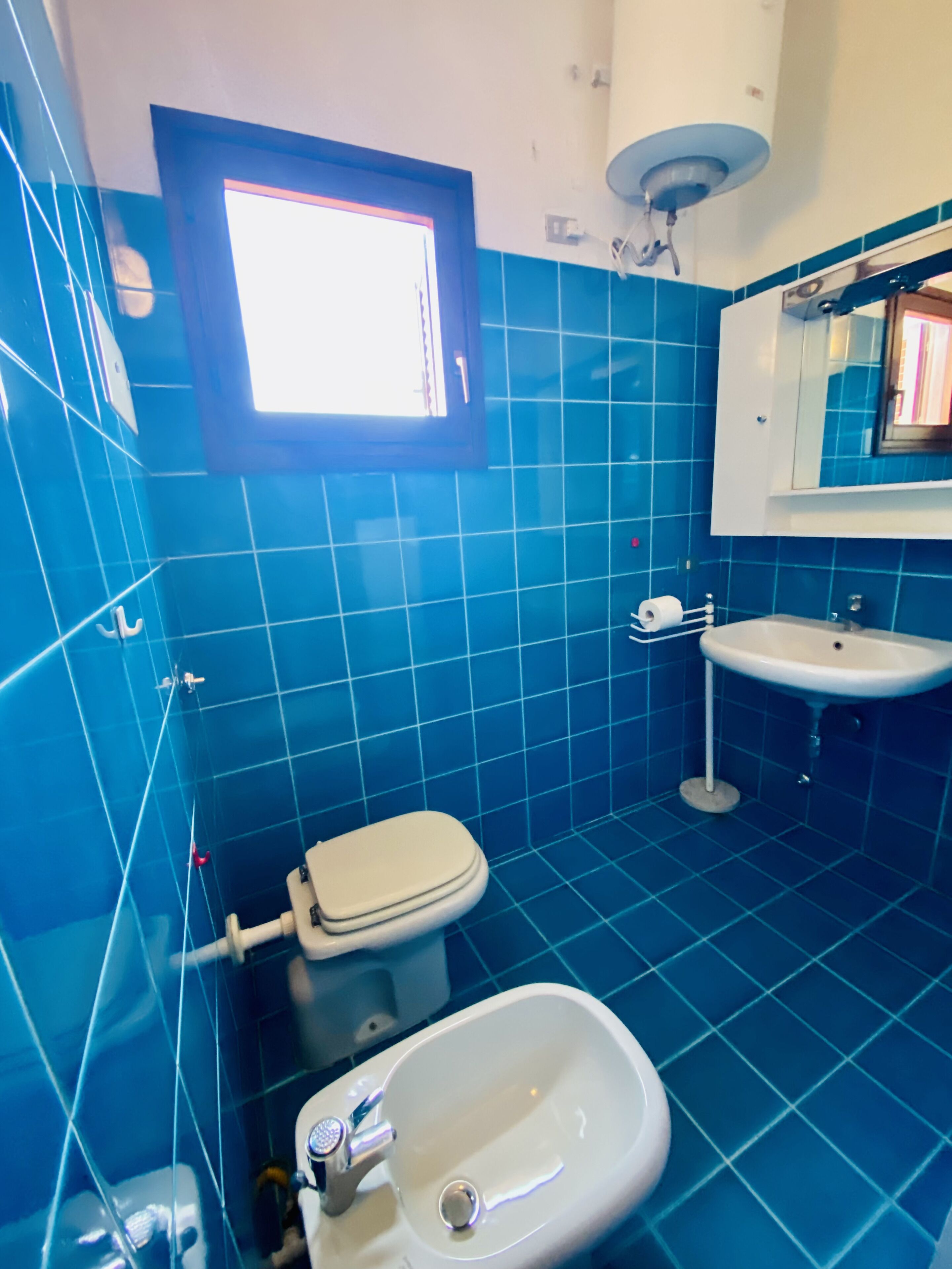 Une salle de bain avec des carreaux bleus, des toilettes, un lavabo et une fenêtre.