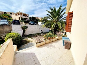 Une cour intérieure d’une résidence, avec un patio carrelé, un palmier et un mur blanc percé d’une fenêtre.