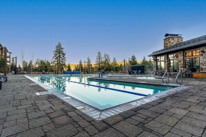 A rectangular swimming pool with clear blue water, surrounded by a paved deck.