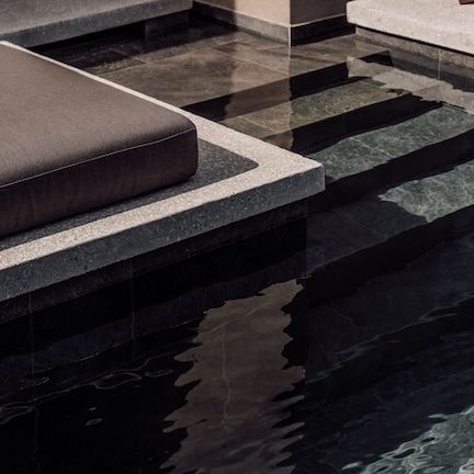 A pool area with steps leading into the water, a bench, and a stone wall.
