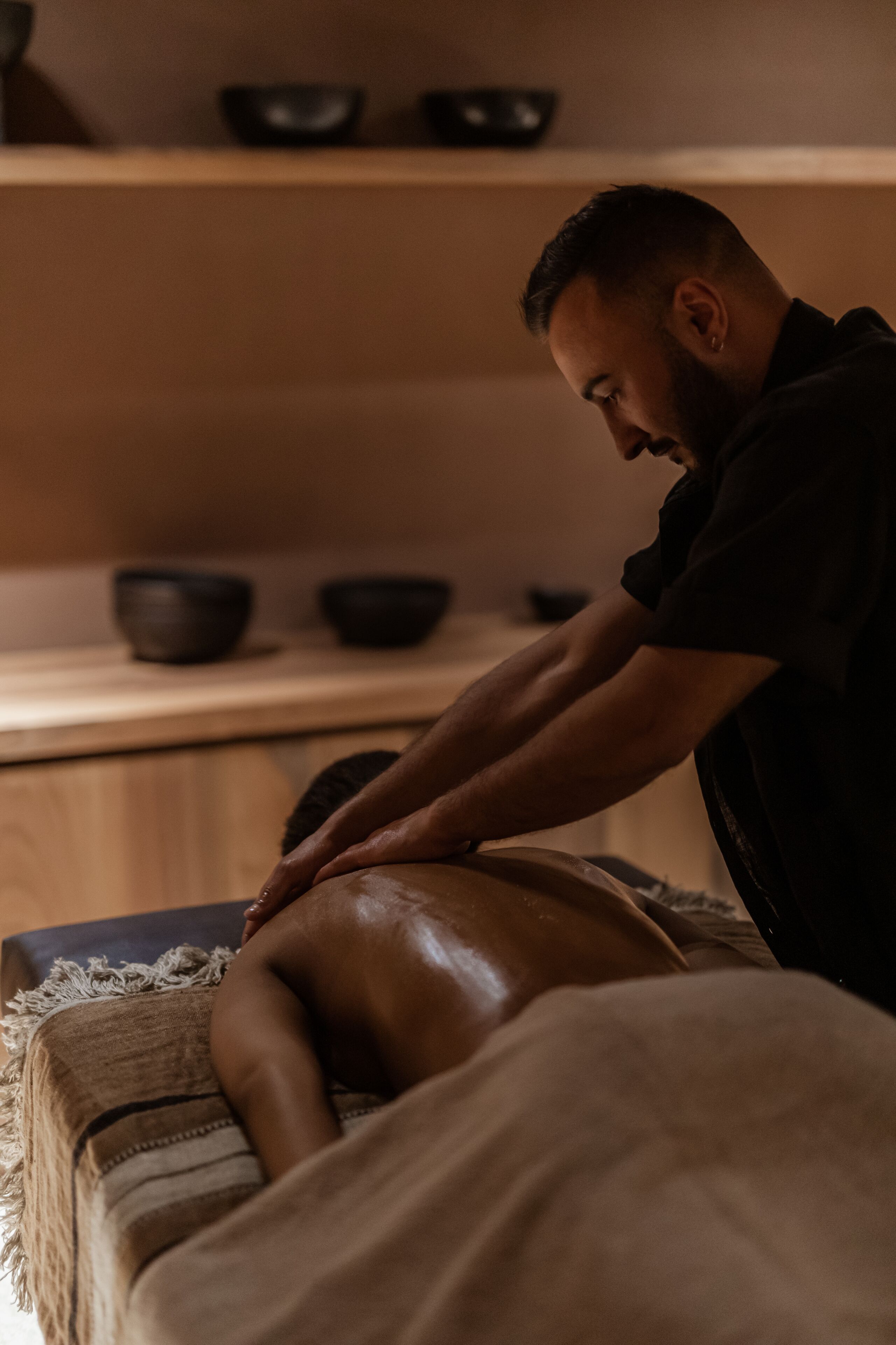 A massage therapy session in a room with wooden furniture and a shelf with bowls.