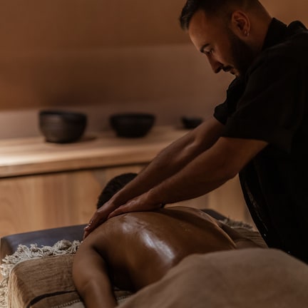 A massage therapy session in a room with wooden furniture and a shelf with bowls.