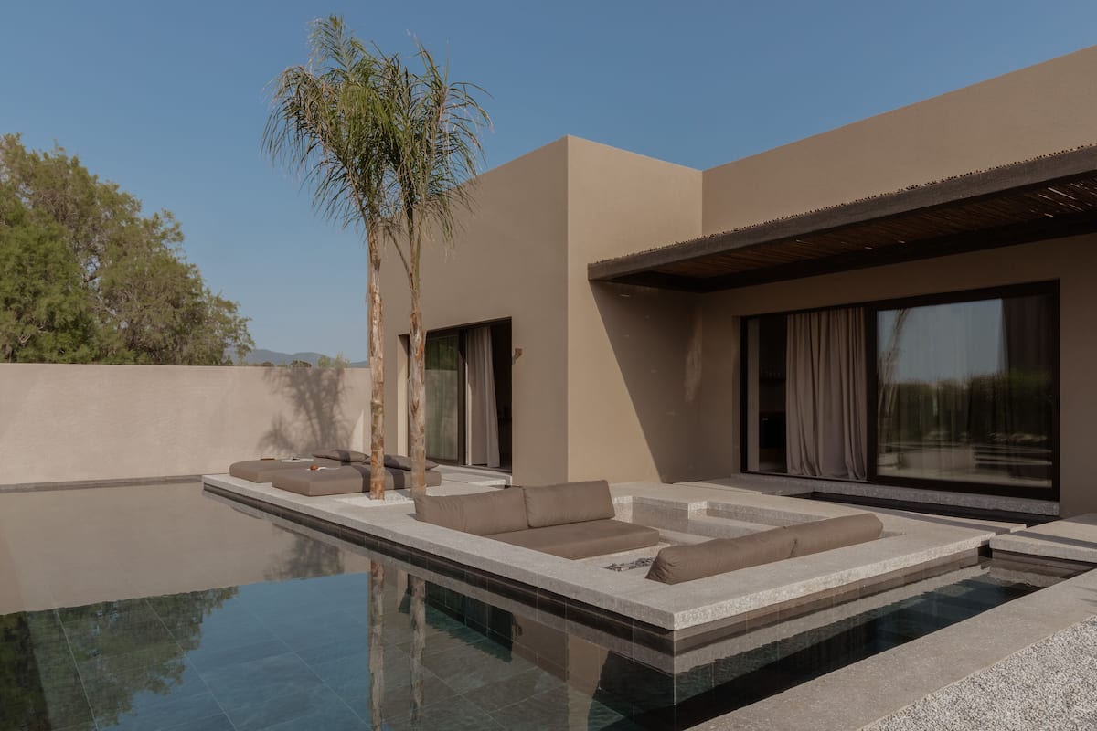 A modern outdoor pool area with a minimalist design, including a seating area with cushions and a palm tree.
