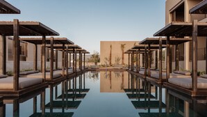 A pool area with wooden pergolas and cushioned seating.