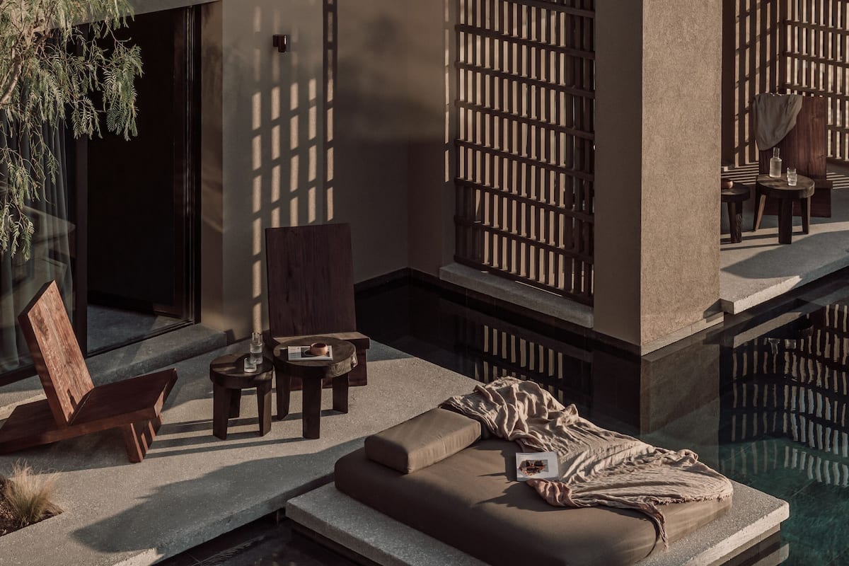 A modern outdoor seating area with a pool, wooden furniture, and a stone bench.