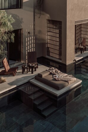 A modern outdoor seating area with a pool, wooden furniture, and a stone bench.