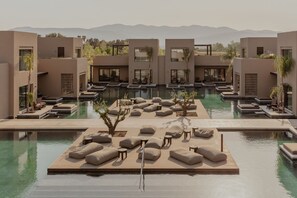 Un resort moderno con piscina central, zonas de descanso y vistas a la montaña.