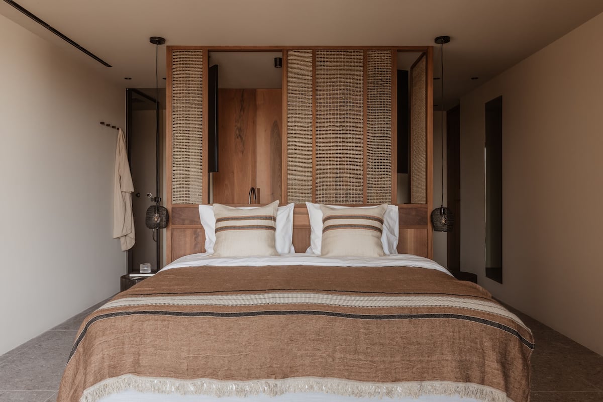 A modern bedroom with a large bed, wooden headboard, and a view of the bathroom.