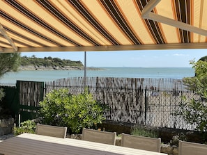 Un espace extérieur aménagé, abrité et doté de sièges, offrant une vue sur la mer, avec une clôture en bambou et de la verdure.