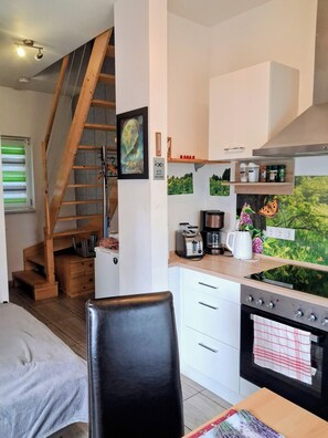 A compact kitchen with a built-in oven, a coffee maker, and a toaster. There is a wooden staircase leading to an upper level. - Guesthouse Rand Berlin-Sonnenblume 3 adults or2 adults+2 children up to 12 years (Rüdersdorf OT Tasdorf)