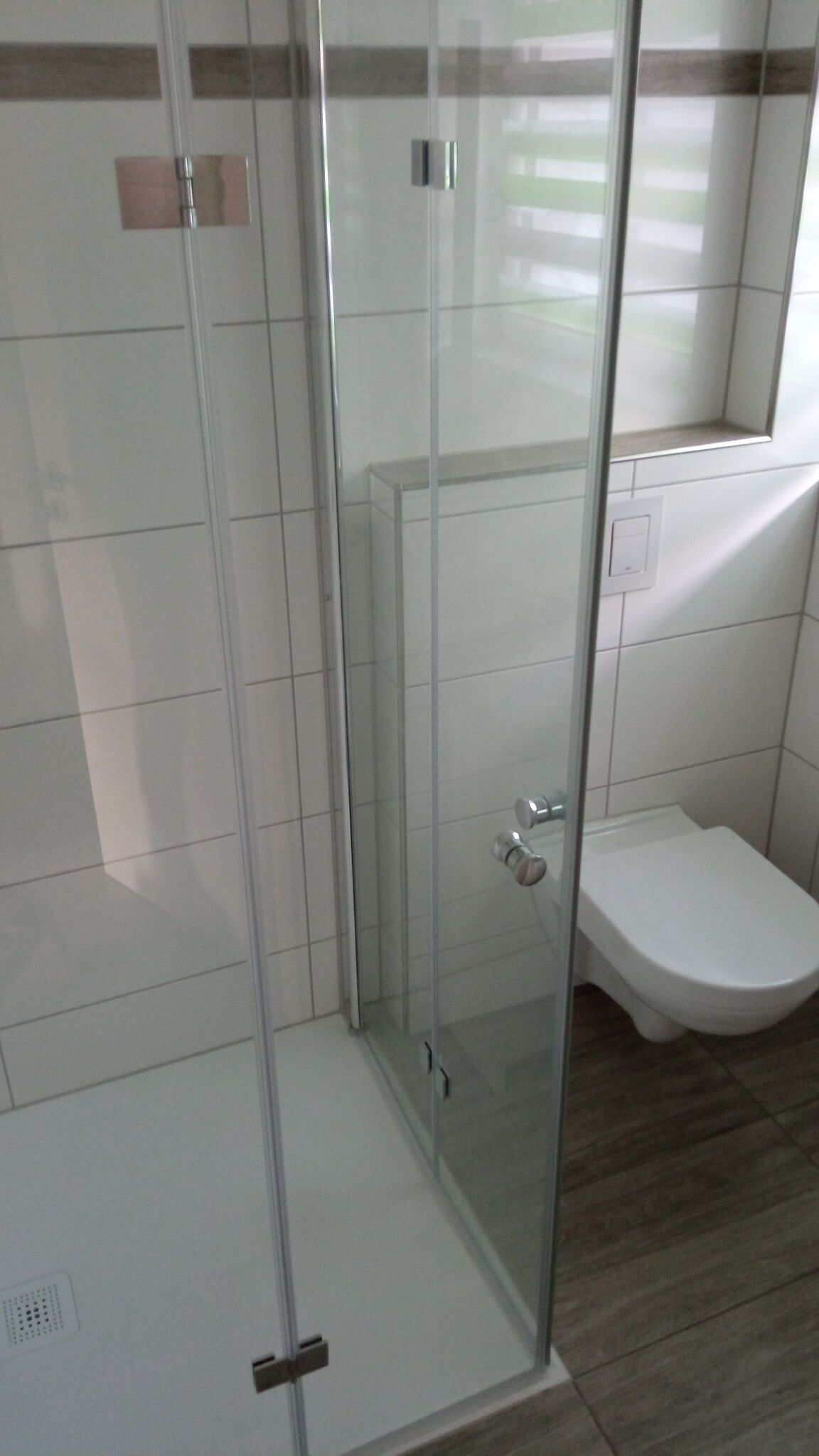 Un bagno moderno con cabina doccia in vetro, un WC bianco e pavimento piastrellato.