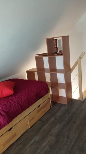 A bedroom with a wooden bed, a red pillow, a wooden nightstand with a vase, and a staircase.