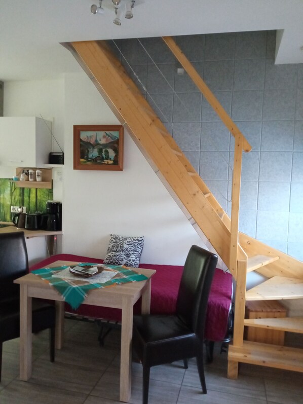 Een eetruimte met een houten tafel, stoelen en een rode bank. Achtergrond toont een trap met houten leuningen.
