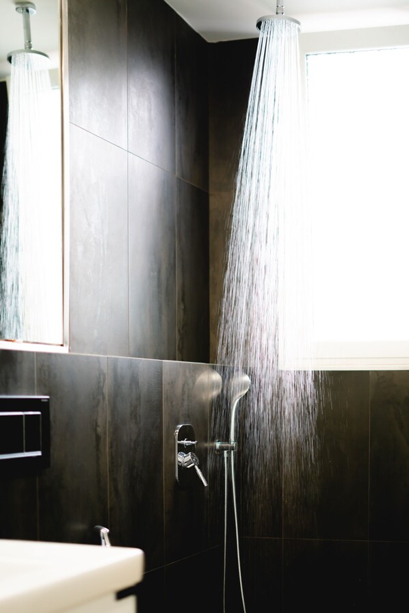 A modern bathroom with a shower head, dark tiles, and a window. - Glyfada Luxury Residence (Glyfada)
