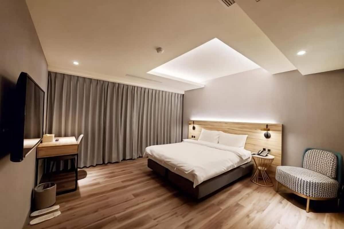 A modern hotel room with a large bed, a desk, a chair, and a television.