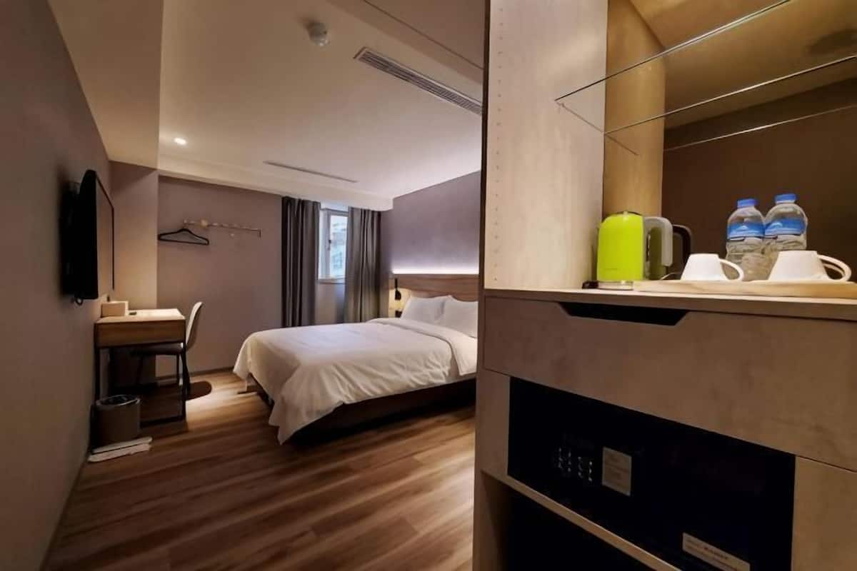 A hotel room with a bed, desk, chair, and a mirror.