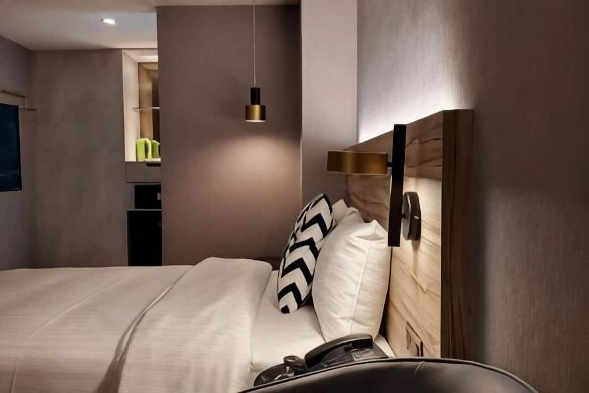 A modern hotel room with a bed, bedside table, and a hanging light fixture.