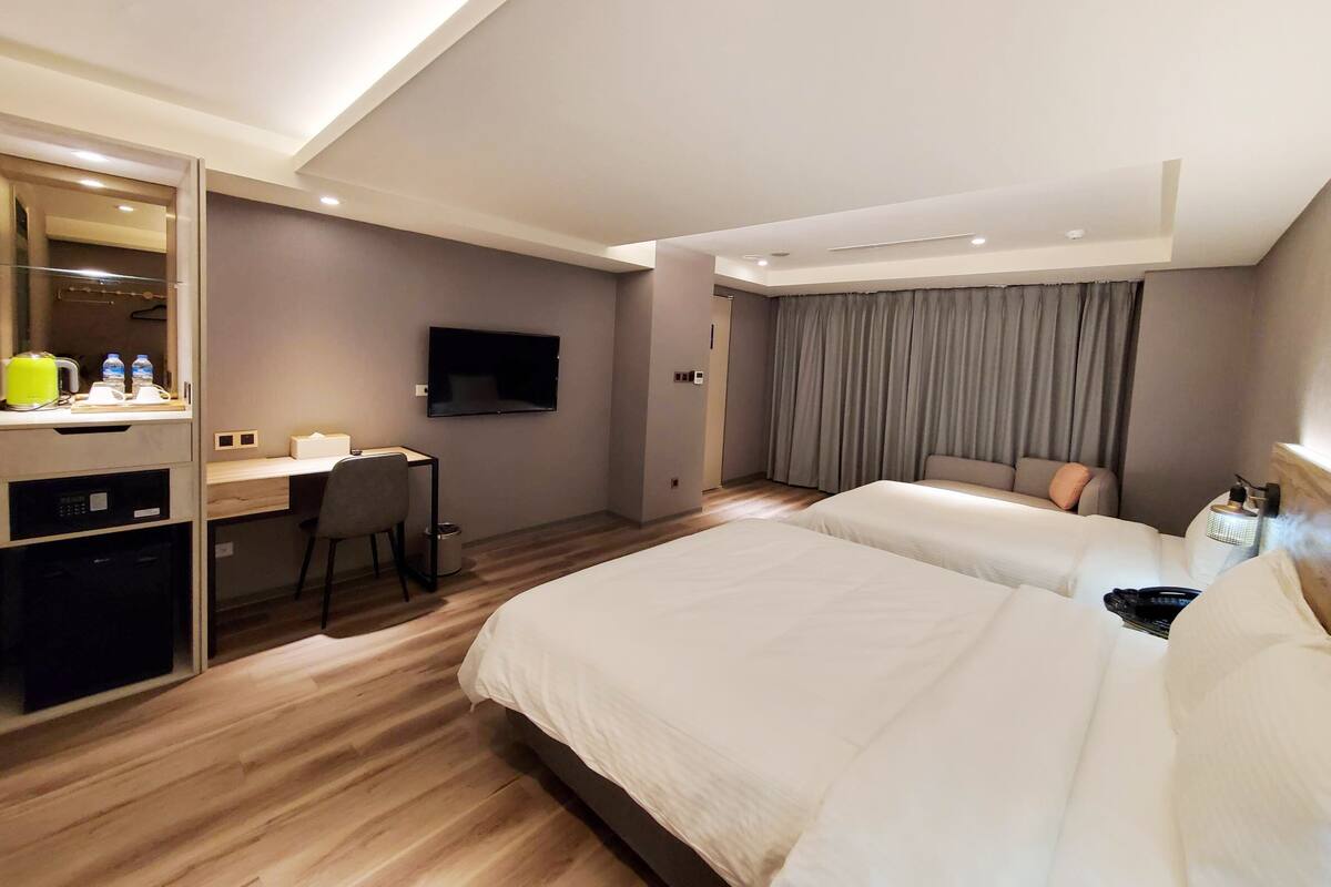 A hotel room with two beds, a desk with a chair, a flat-screen TV, and a large mirror.