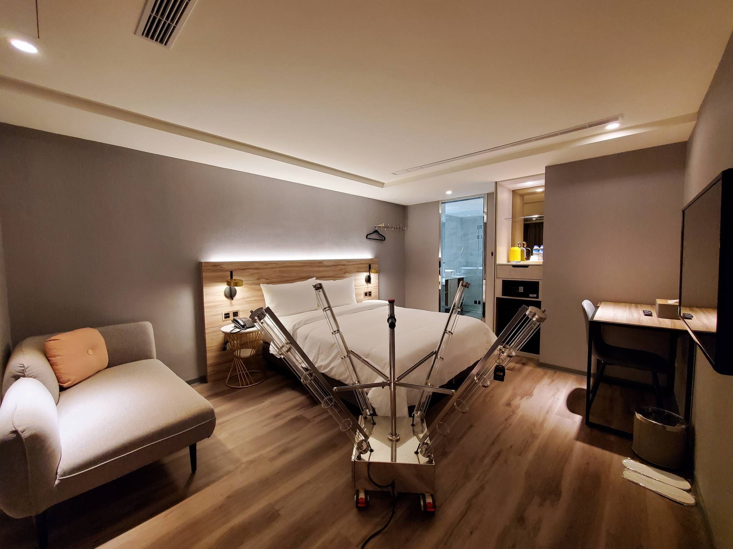 A modern hotel room with a large bed, bedside tables, a sofa, a desk, and a mirror.