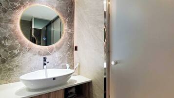 Un baño moderno con pared de mármol, un espejo redondo, un mueble de tocador de madera y un inodoro.