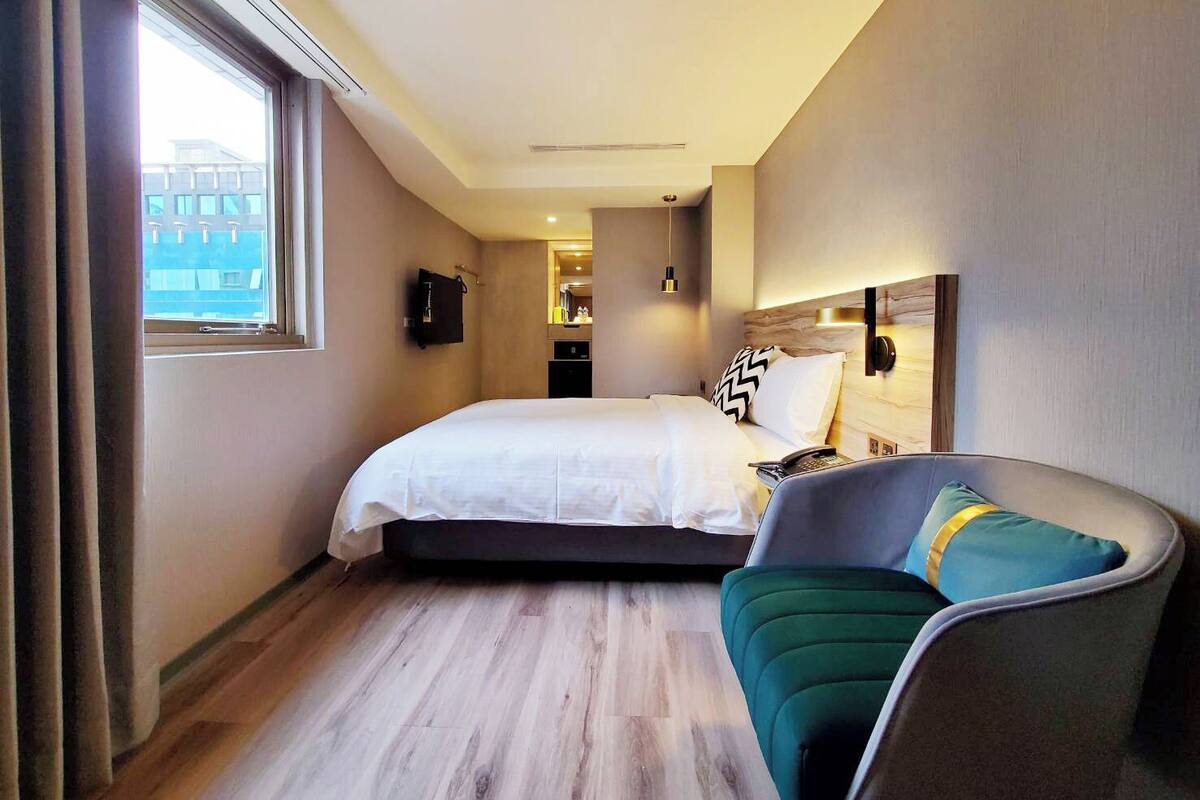 A hotel room with a bed, a chair, a desk, and a window.