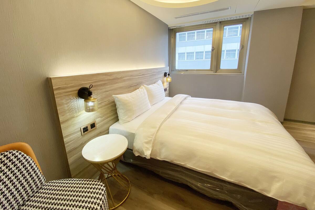 A modern hotel room with a large bed, a small round table, and a houndstooth chair.