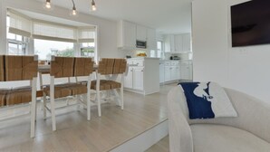 Ein modernes Wohnzimmer mit einer Couch, einem Essbereich mit Tisch und Stühlen sowie einer Küche mit weißen Schränken.