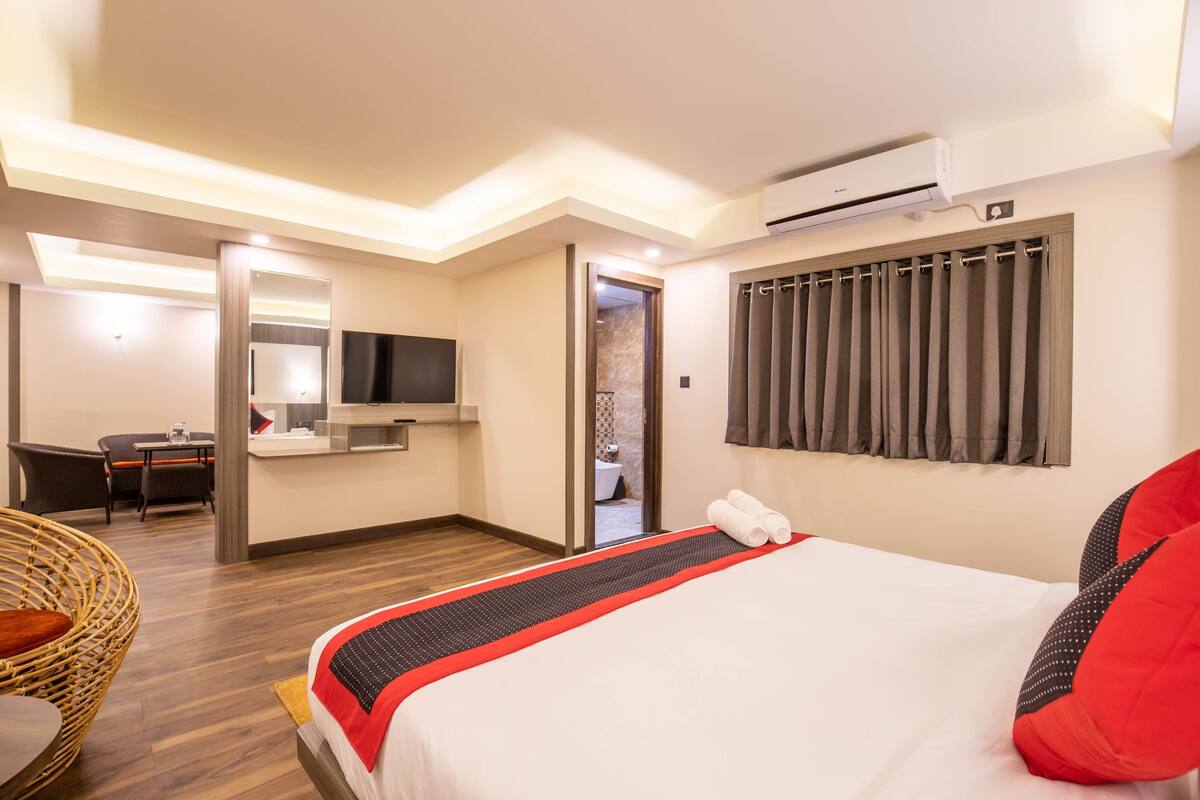 A hotel room with a bed, a desk, a chair, a television, and an air conditioning unit.