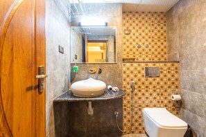 A bathroom with a wooden door, a sink with a mirror, a toilet, and a shower area with tiled walls. - Hotel Wawa (Kathmandu)