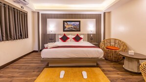Habitación de hotel con cama, aire acondicionado de pared, un cuadro, una silla de mimbre y una mesita.