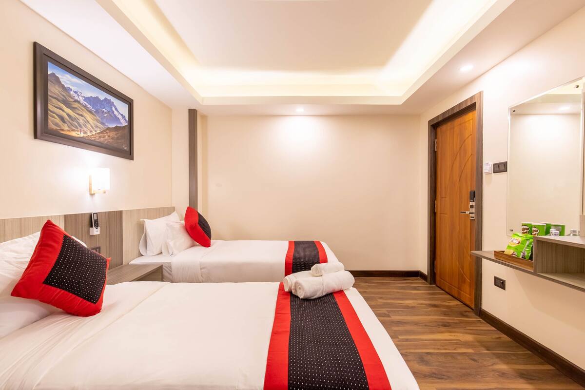 A hotel room with two beds, a wooden door, a mirror, and a painting on the wall.