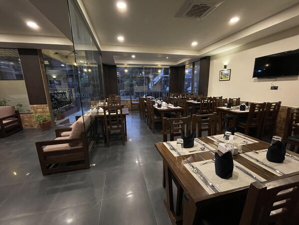 A restaurant with multiple dining tables and chairs, large windows, and a flat-screen TV on the wall. - Hotel Wawa (Kathmandu)