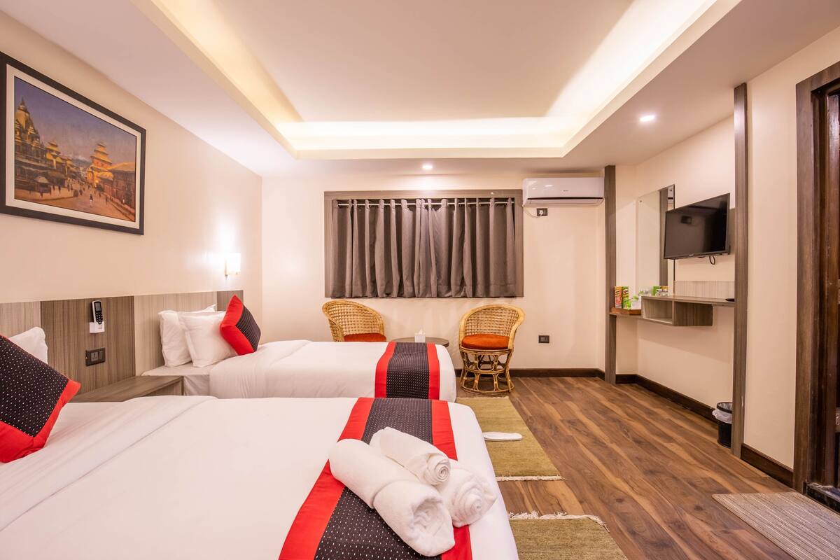 A hotel room with two beds, a television, a painting, and a window with curtains.