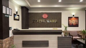 Zona de recepción de hotel con diseño moderno, que incluye un mostrador de recepción, un letrero con el nombre del hotel y un cuadro en la pared.