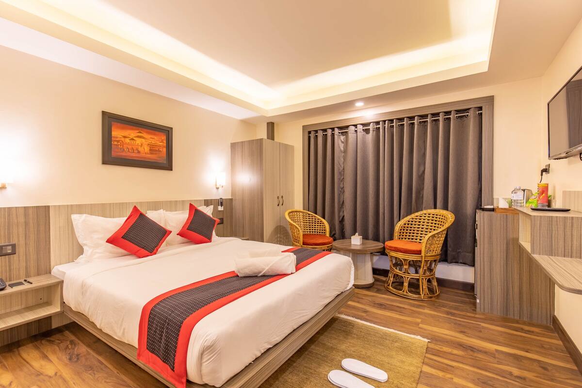 A hotel room with a large bed, two chairs, a small table, and a desk.