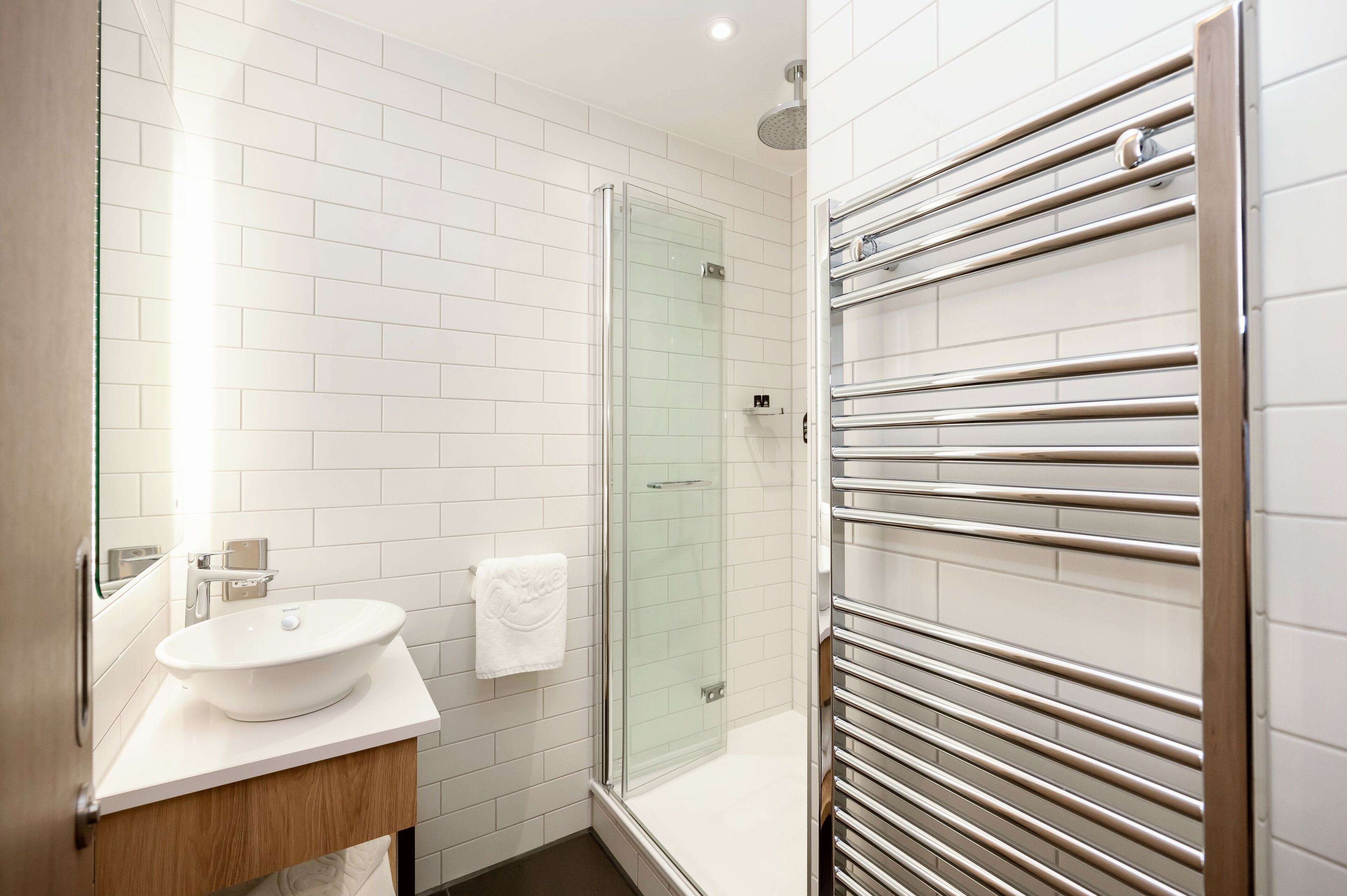 A modern bathroom with a glass shower enclosure, a white sink, and a towel rack.